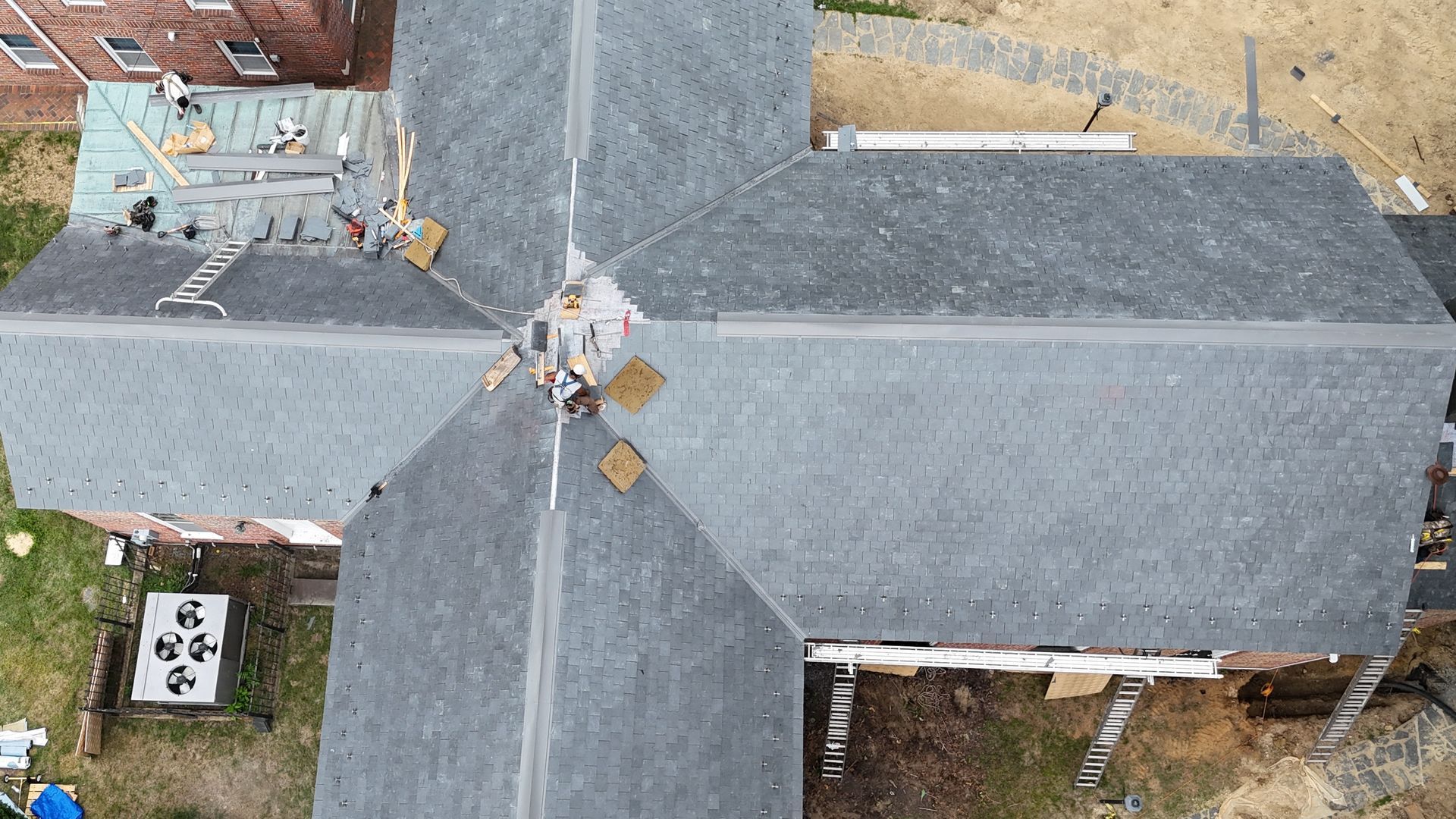 Aerial view of a gray-roofed house with a central chimney and a driveway beside it.