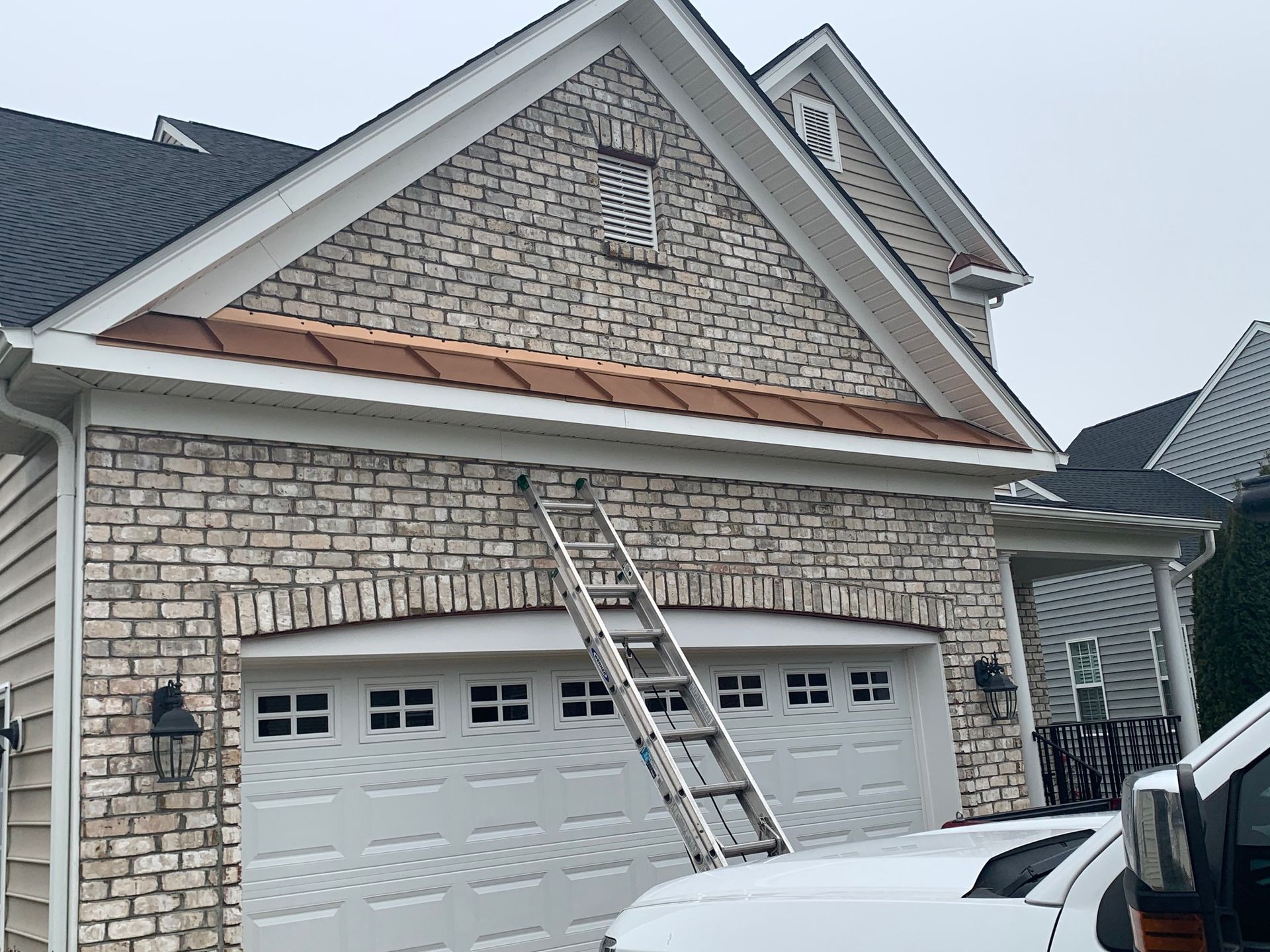 A white truck is parked in front of a brick house with a ladder attached to it.