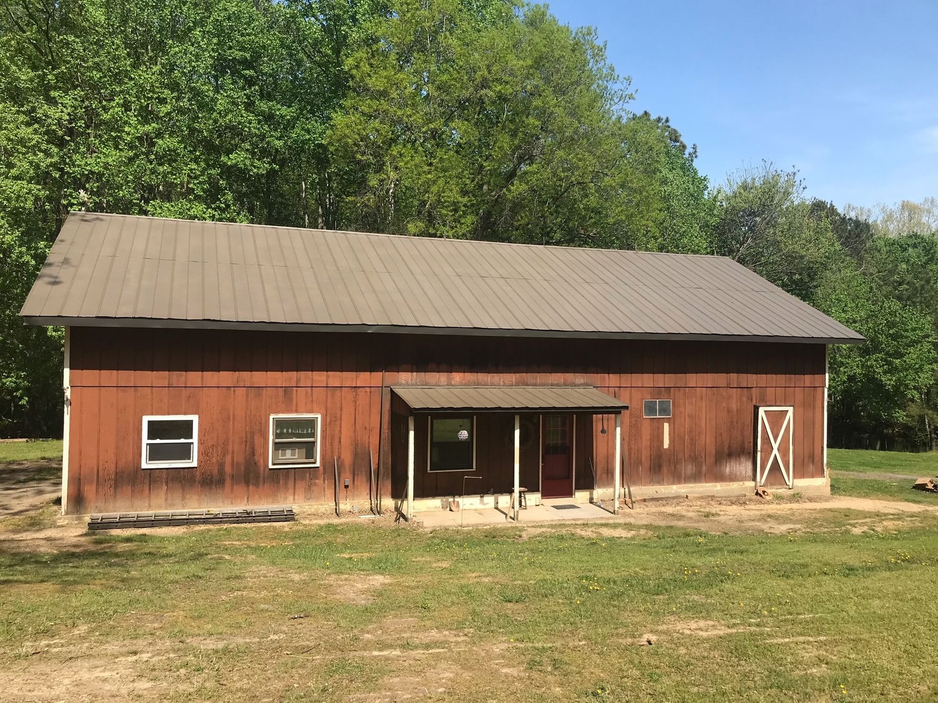 A large red barn with a brown roof is sitting in the middle of a grassy field.