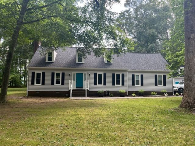 A white house with black shutters and a blue door is surrounded by trees and grass.