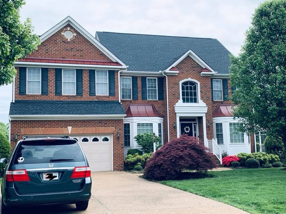 A car is parked in front of a large brick house.