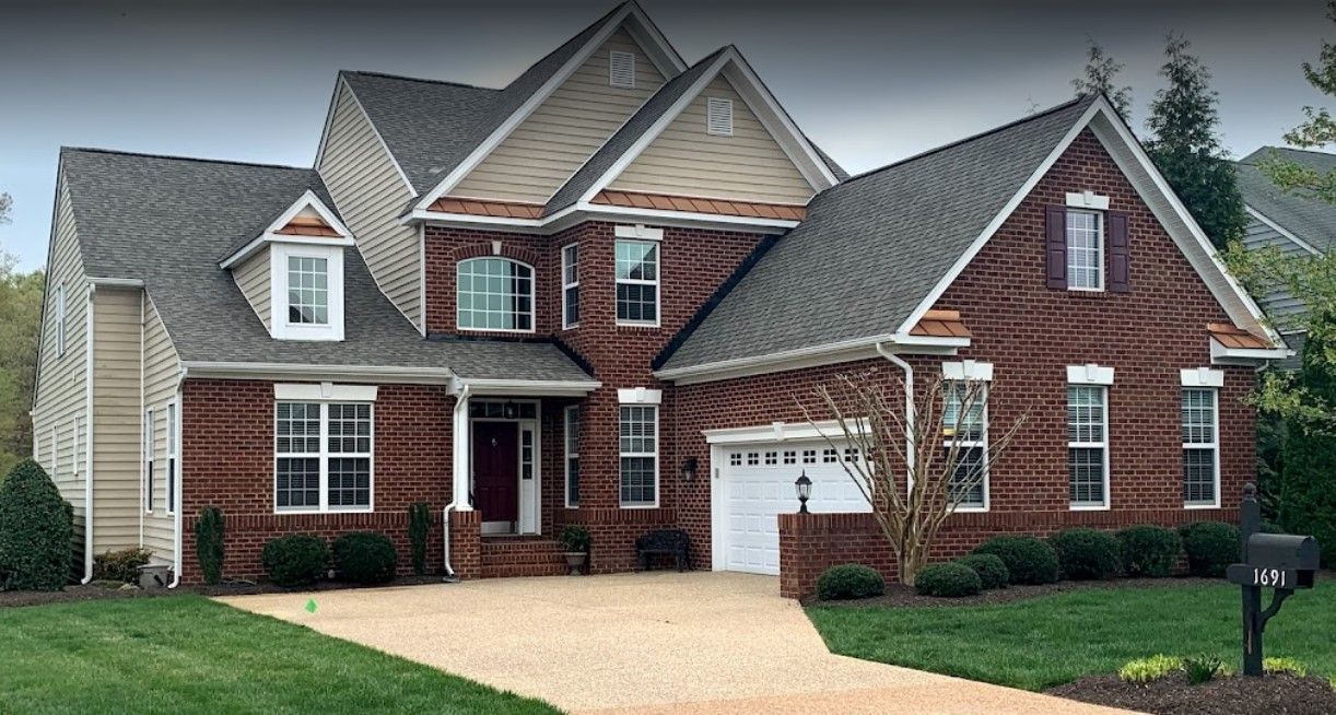 A large brick house with a gray roof is sitting on top of a lush green lawn.