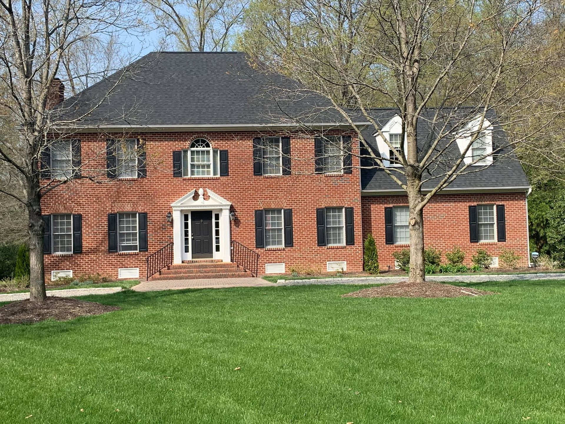A large brick house with black shutters is sitting on top of a lush green lawn.
