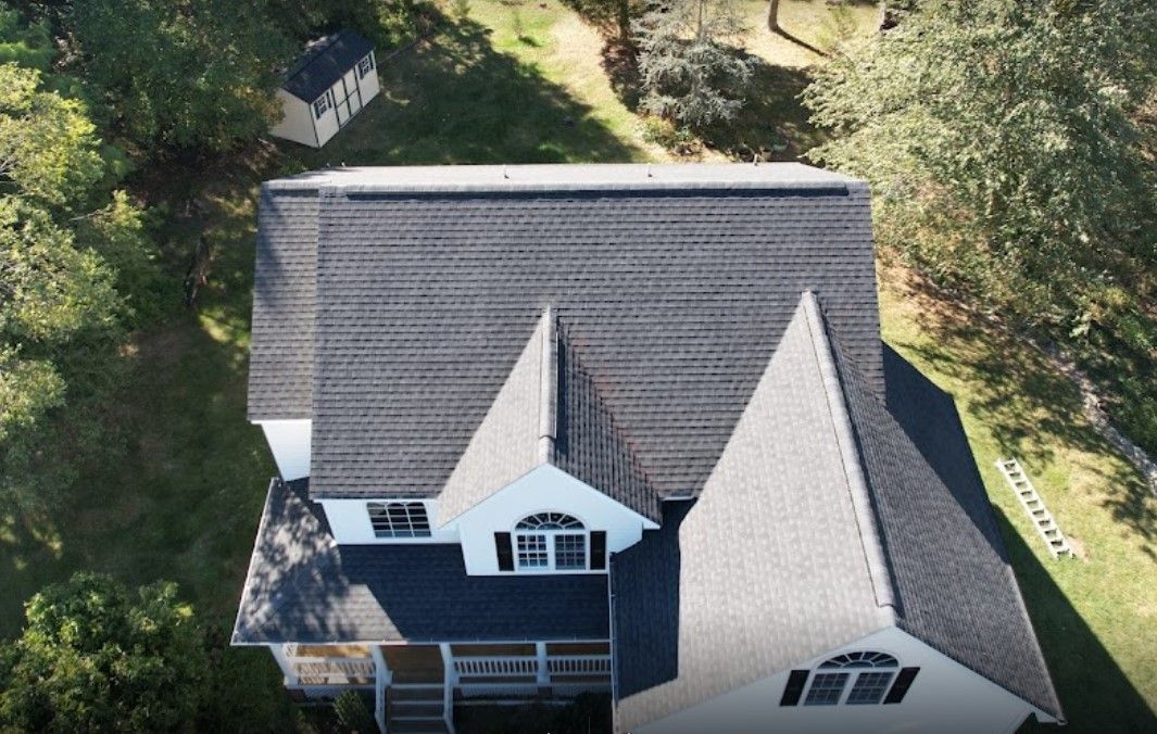 An aerial view of a large white house with a black roof surrounded by trees.