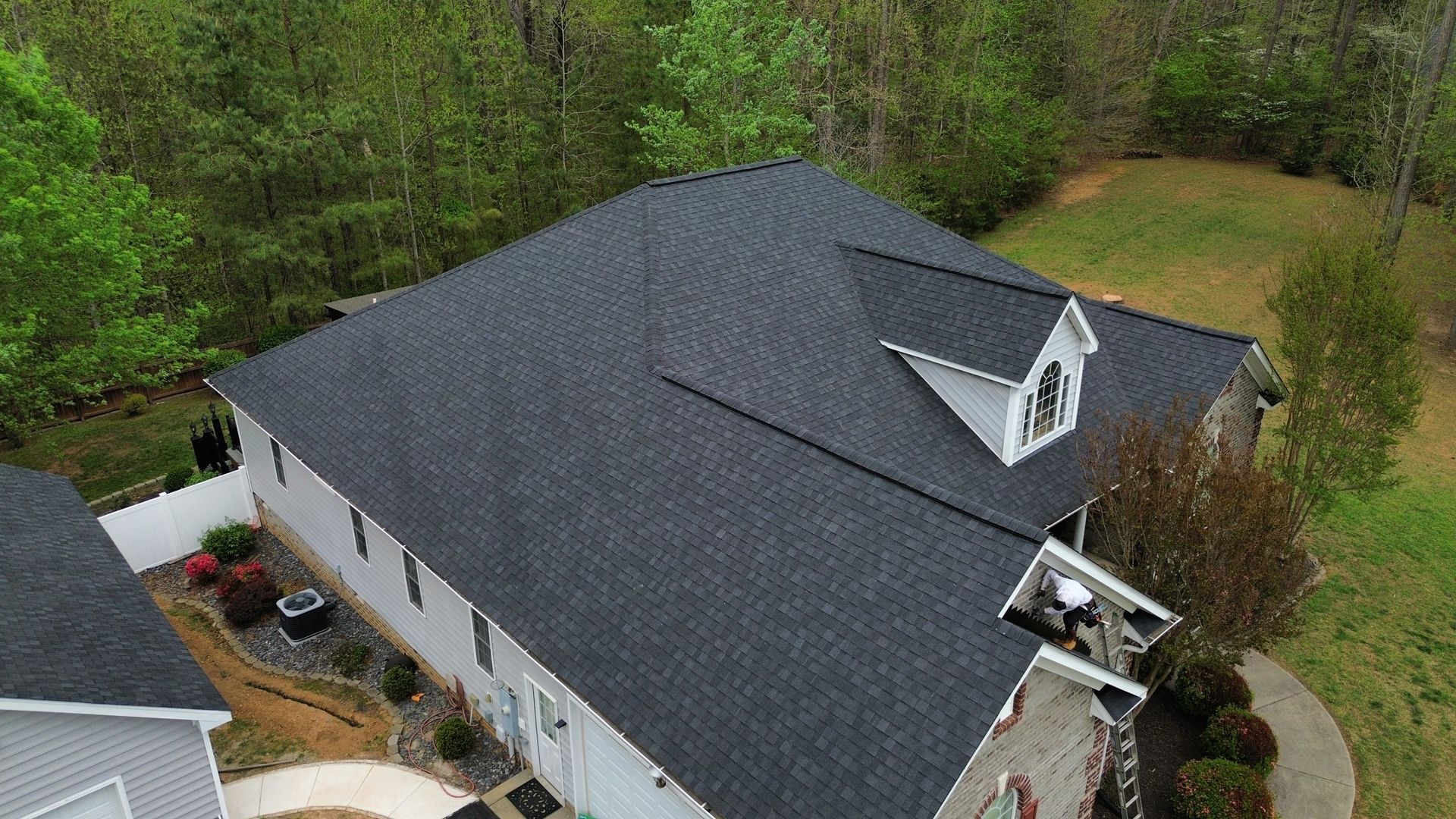 Aerial view of a house with a dark gray roof surrounded by trees and a grassy yard.