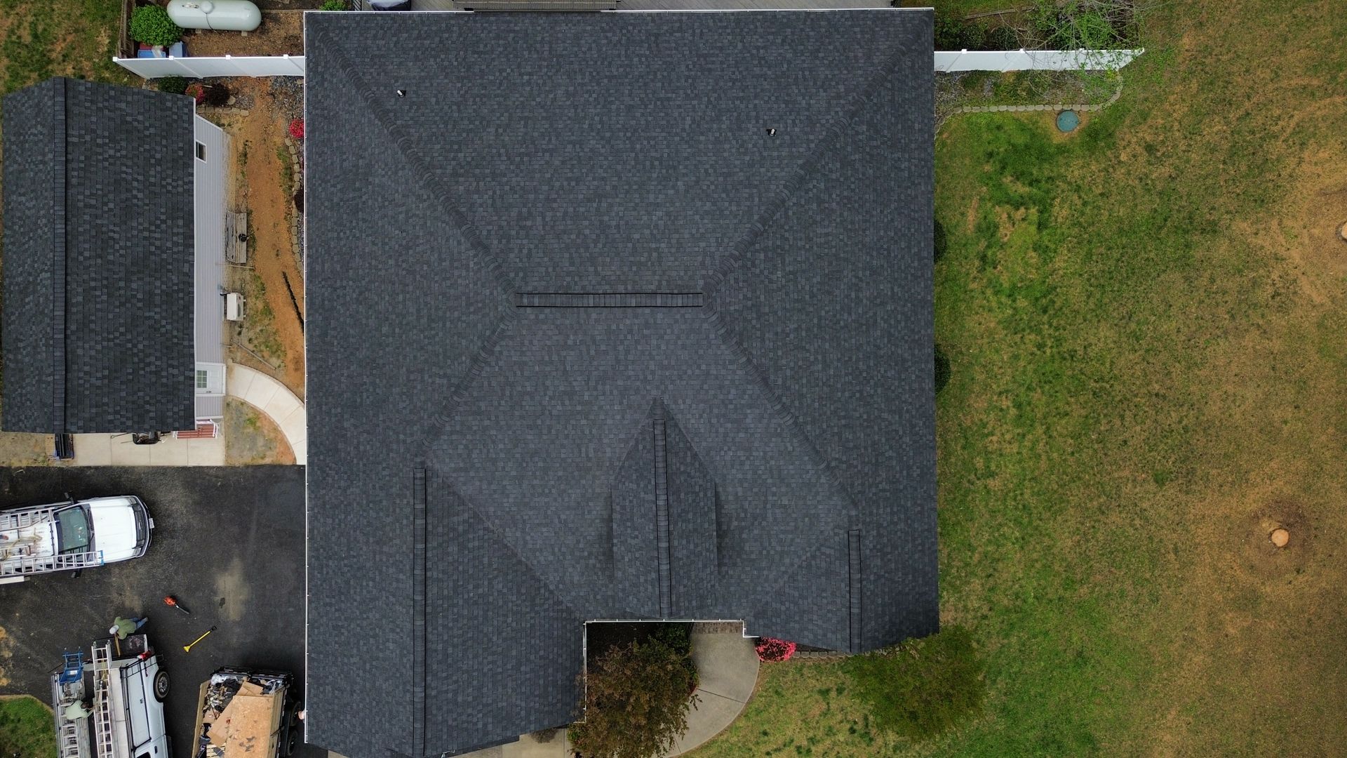 Aerial view of a dark gray-roofed house with lawn and a driveway beside it.
