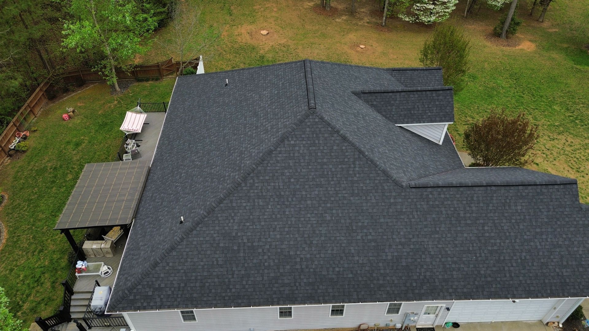 Aerial view of a gray-roofed house surrounded by trees and lawn.