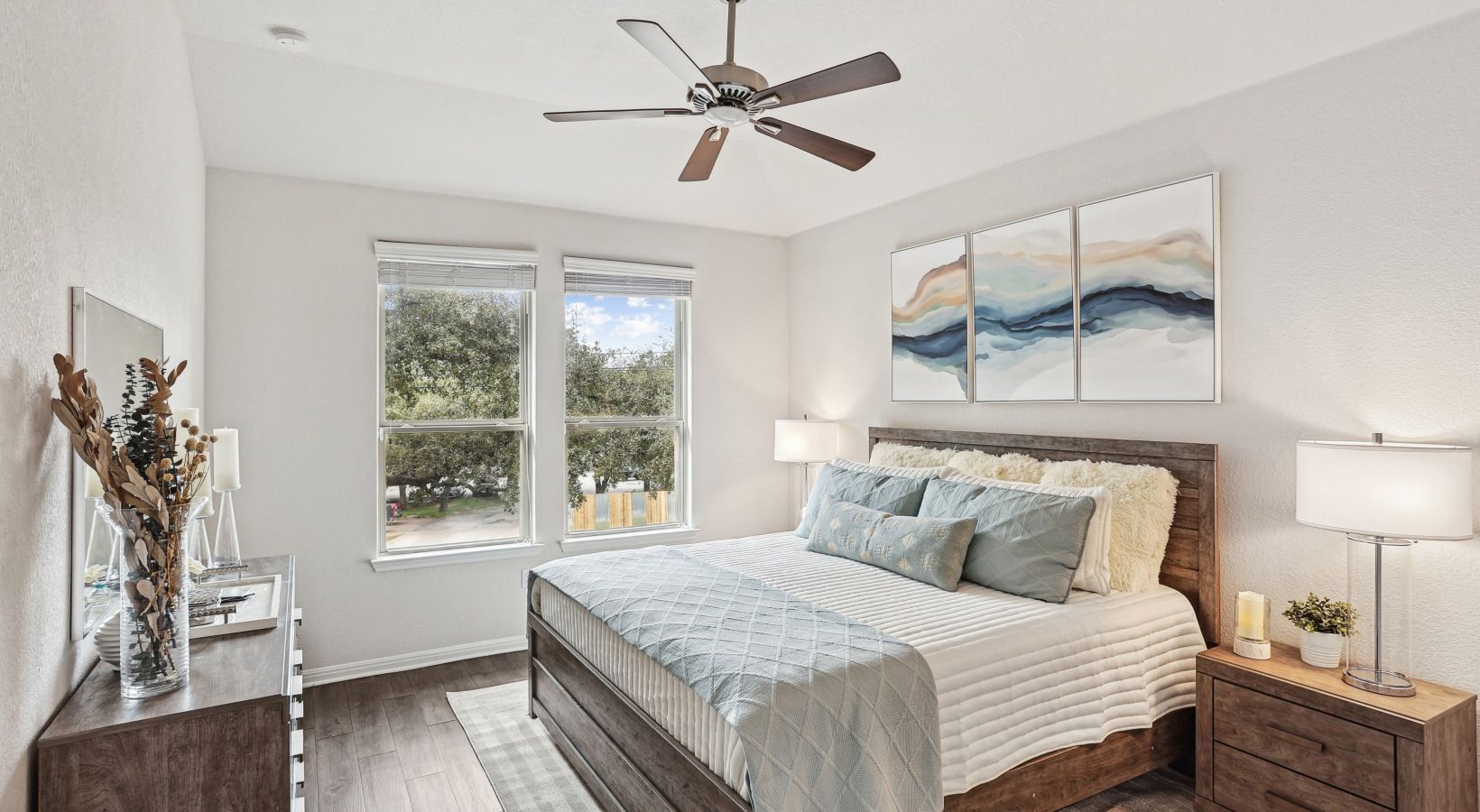 Bedroom with a wooden bed, two nightstands, ceiling fan, and large windows with abstract art.