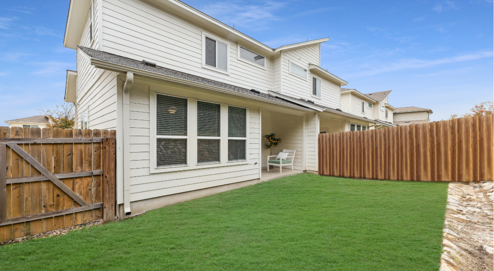 Backyard of a white two-story townhouse with a green lawn, wooden fence, and a small covered patio.