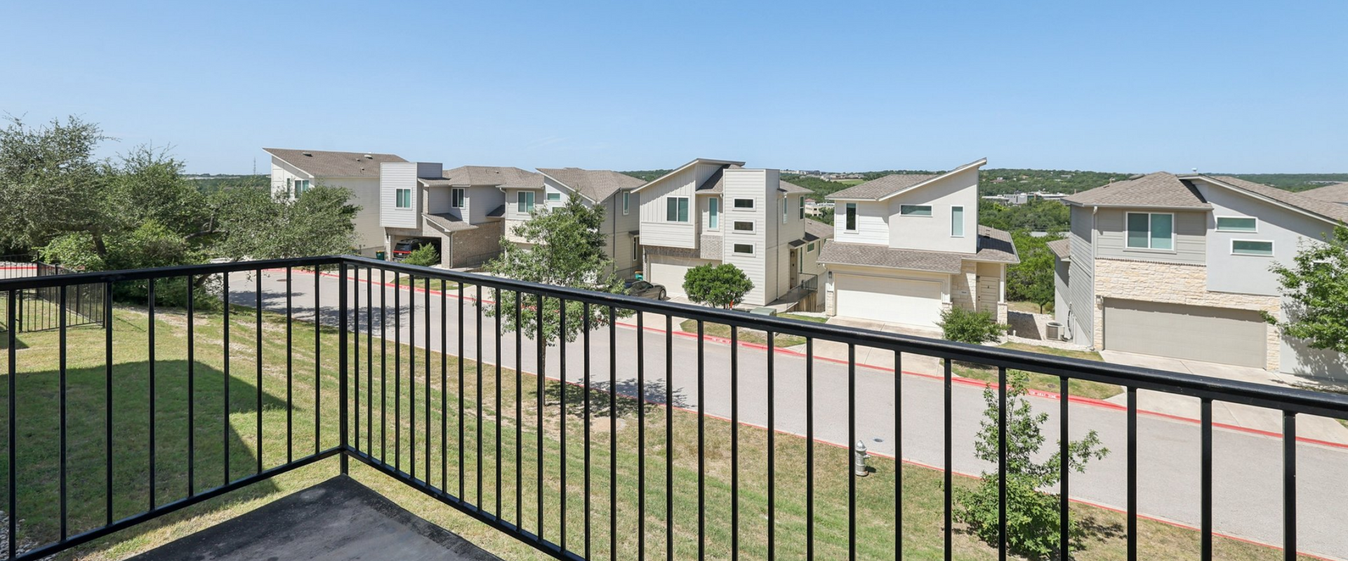 View from a balcony overlooking a neighborhood with modern houses and a blue sky.