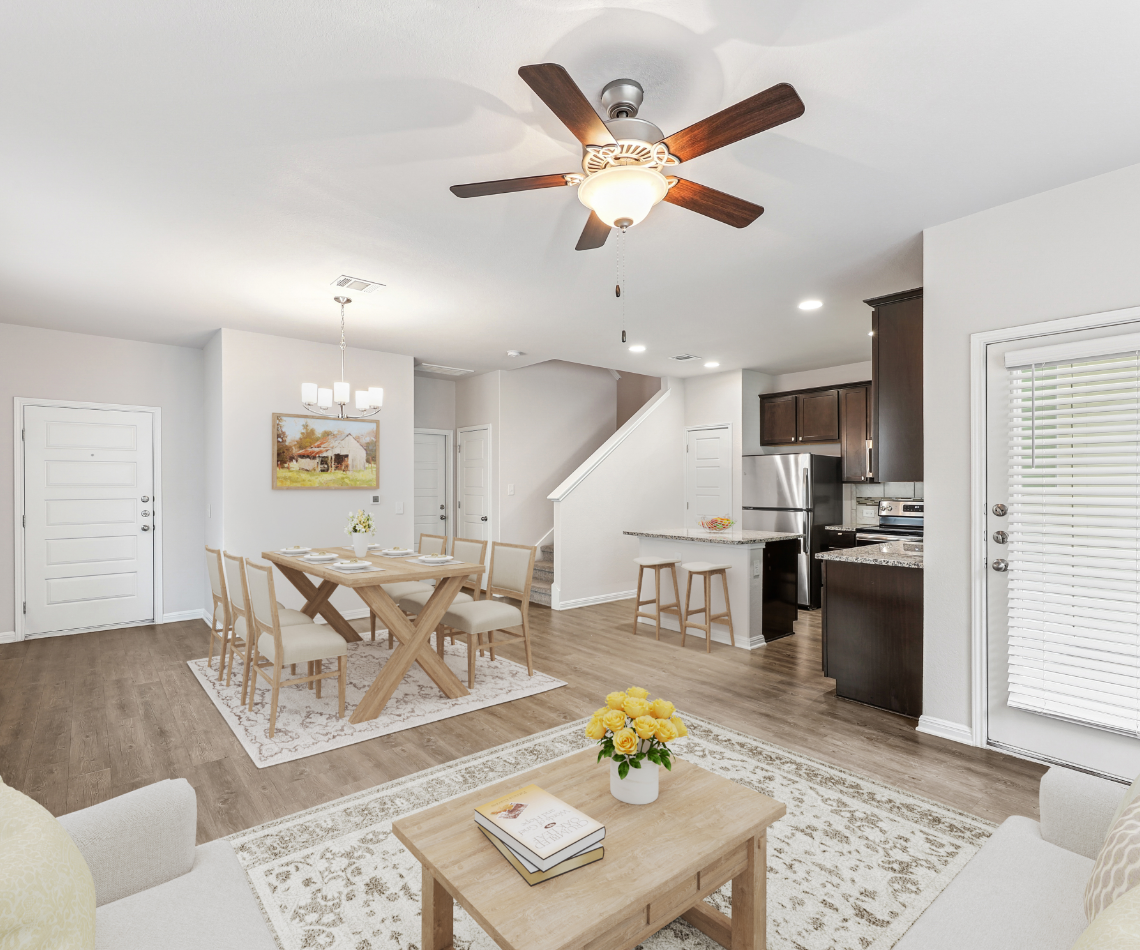 Open-concept living space with dining, kitchen, and living areas. Brown ceiling fan, light wood floors, neutral walls.