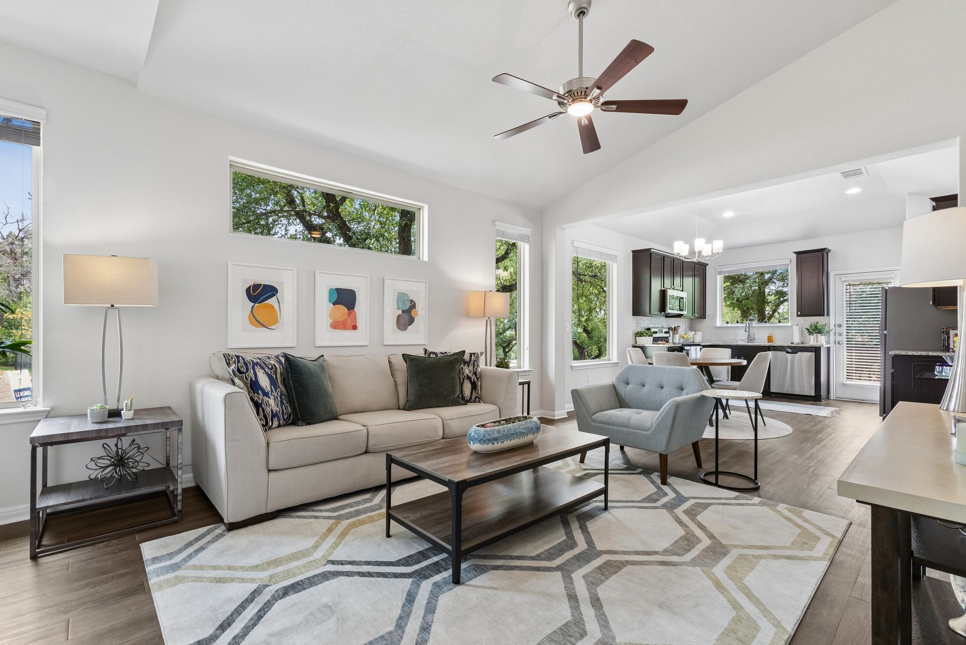Bright modern living room with beige sofa, patterned rug, glass coffee table, and ceiling fan.