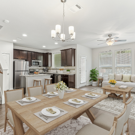 Open-concept dining and living area. Dining table set for six, leads to kitchen and living room with sofa, windows.
