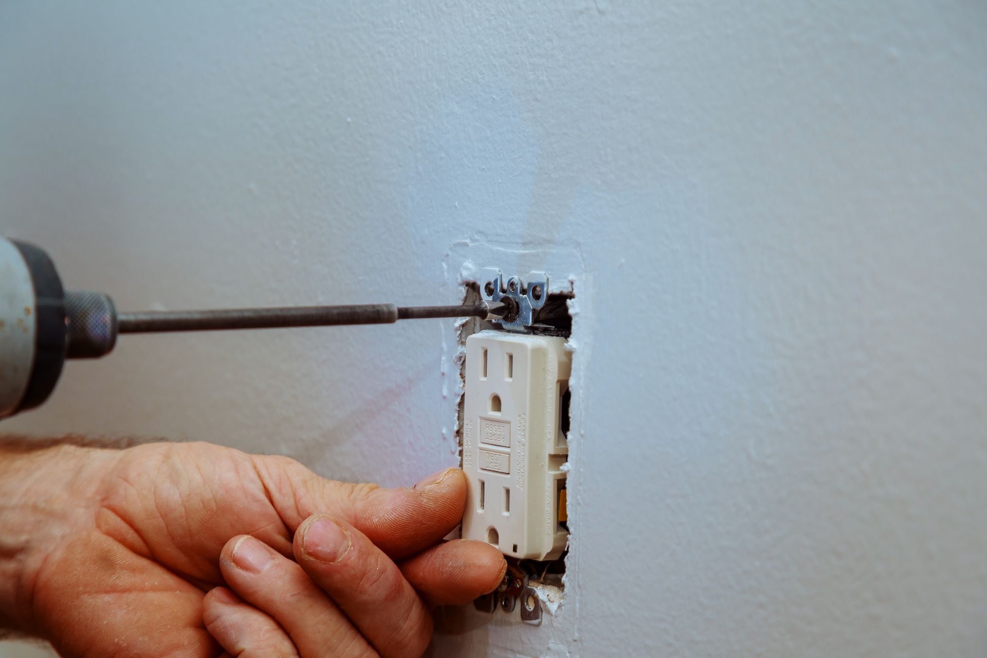 Une personne installe une prise électrique dans un mur avec une perceuse.