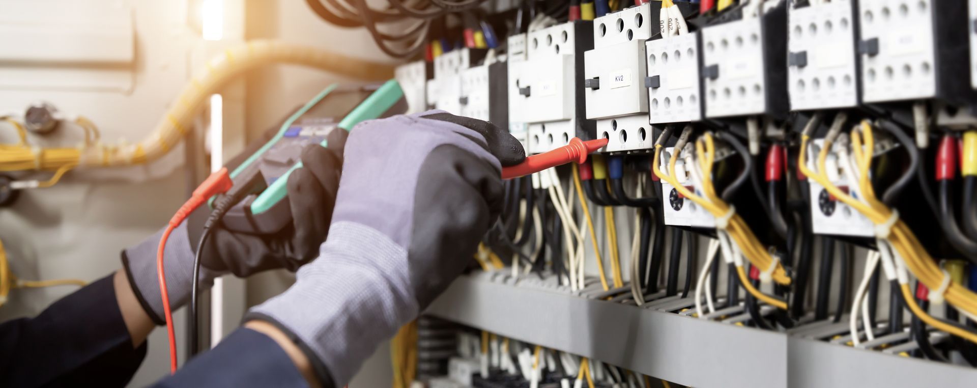 Un électricien travaille sur un panneau électrique avec un multimètre.