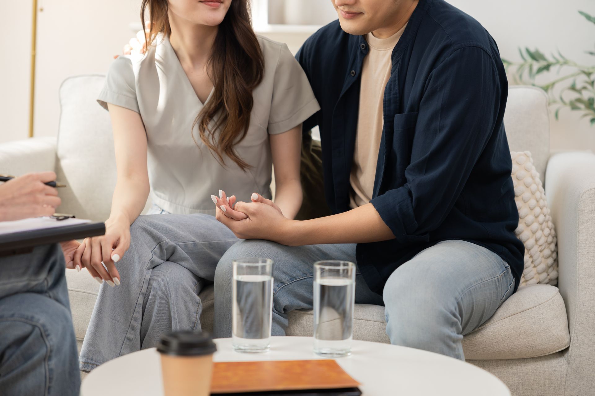 A man and a woman are sitting on a couch holding hands.