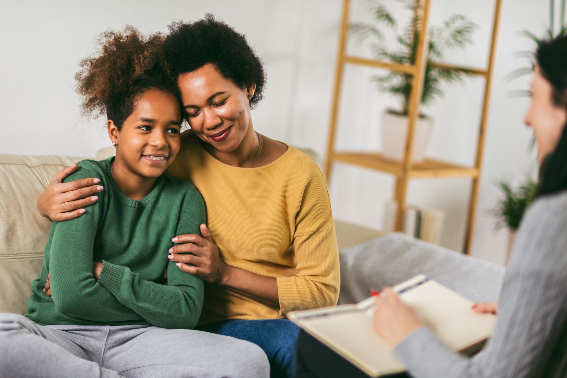 A mother and daughter are sitting on a couch talking to a counselor.