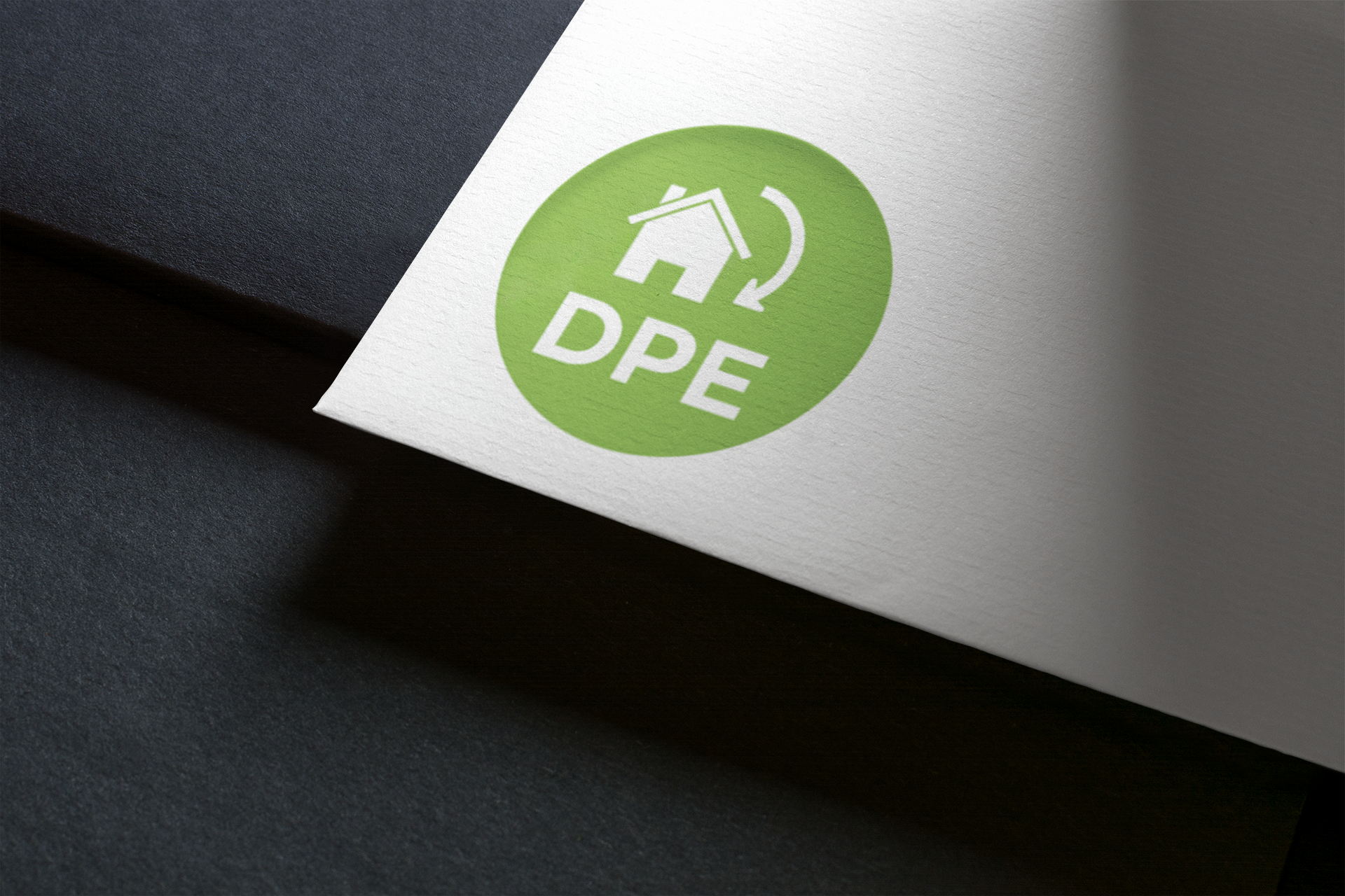 Logo DPE vert avec une maison et des flèches sur papier blanc, en biais sur une surface sombre.