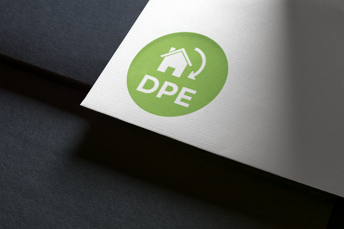 Logo DPE vert avec une maison et des flèches sur papier blanc, en biais sur une surface sombre.