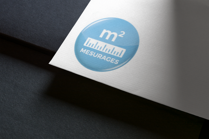 Logo bleu sur papier blanc, avec le texte « m² Mesures » et une icône de règle, sur une surface sombre.
