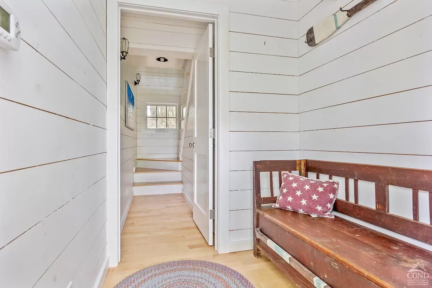 A hallway with a wooden bench and a rug.