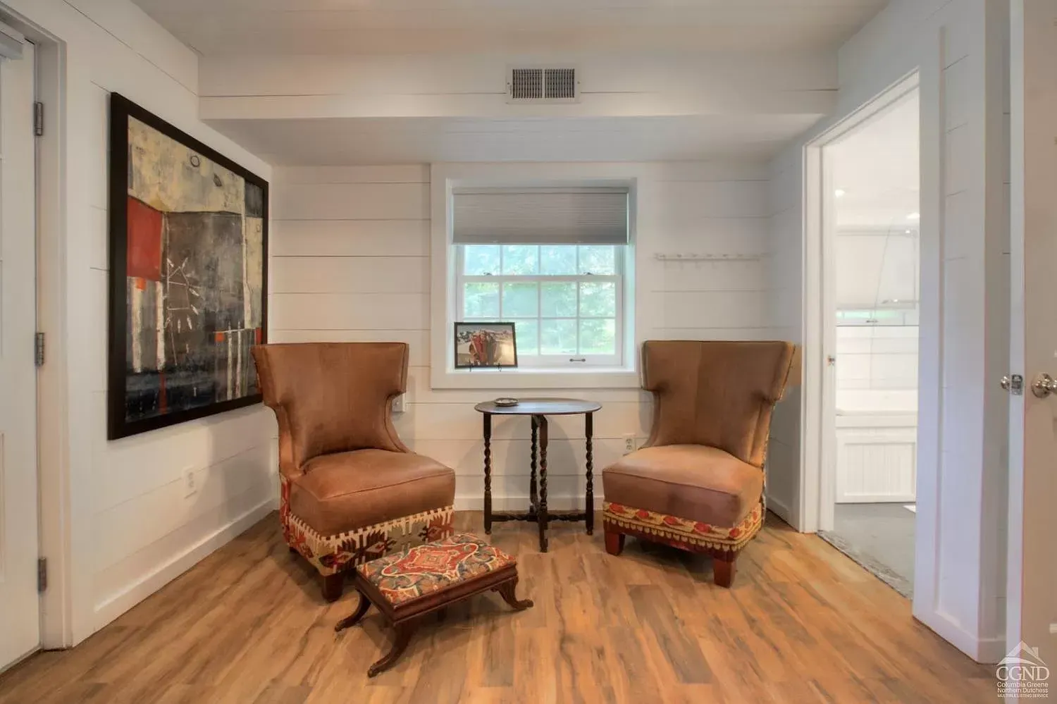 A living room with two chairs , a table and a painting on the wall.
