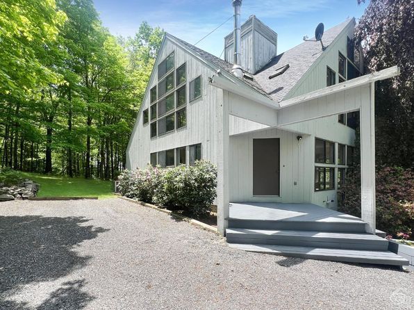 A large white house with stairs leading up to it is surrounded by trees.