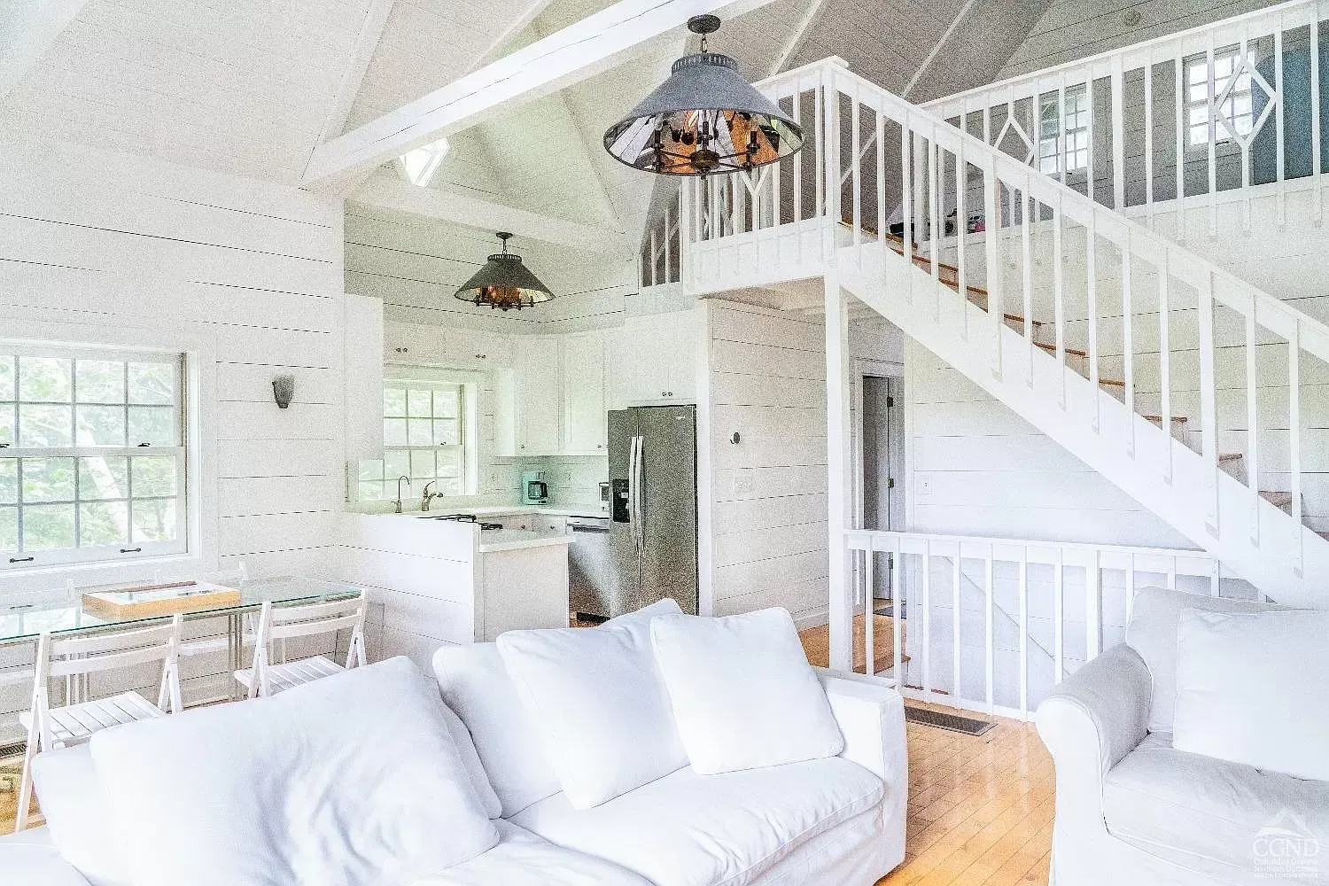 A living room with a white couch , chair , and stairs leading up to the second floor.
