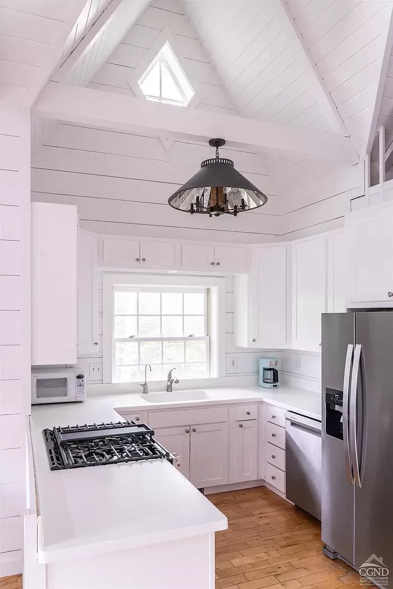 A kitchen with white cabinets , a stove , a refrigerator , and a window.