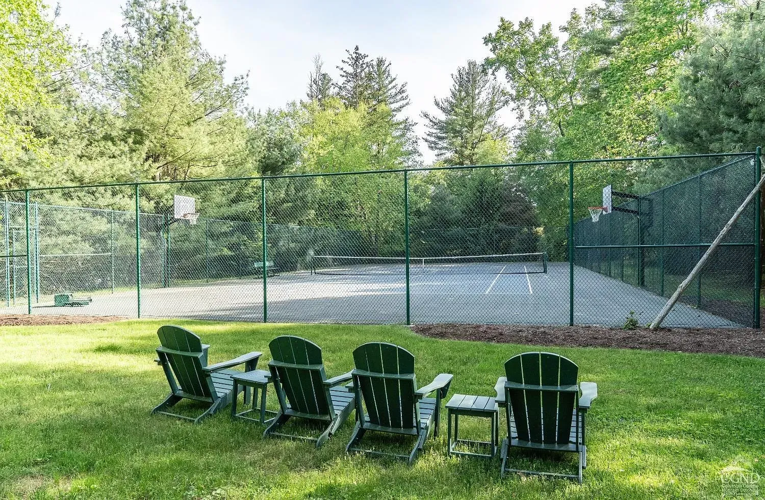 A row of chairs are sitting in the grass in front of a basketball court.