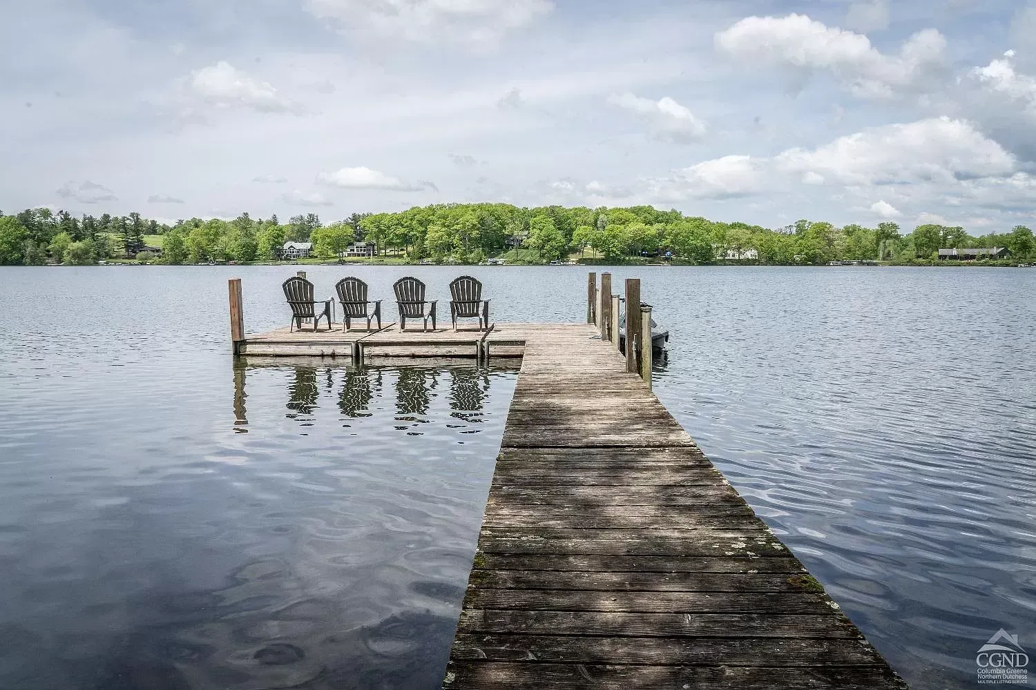 A wooden dock leading to a lake with chairs on it.