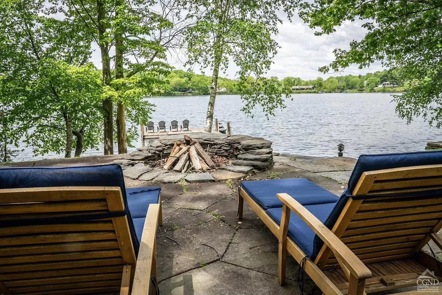 Two lounge chairs are sitting on a patio overlooking a lake.