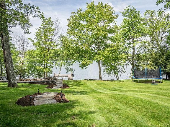 There is a trampoline in the middle of a lush green field surrounded by trees.