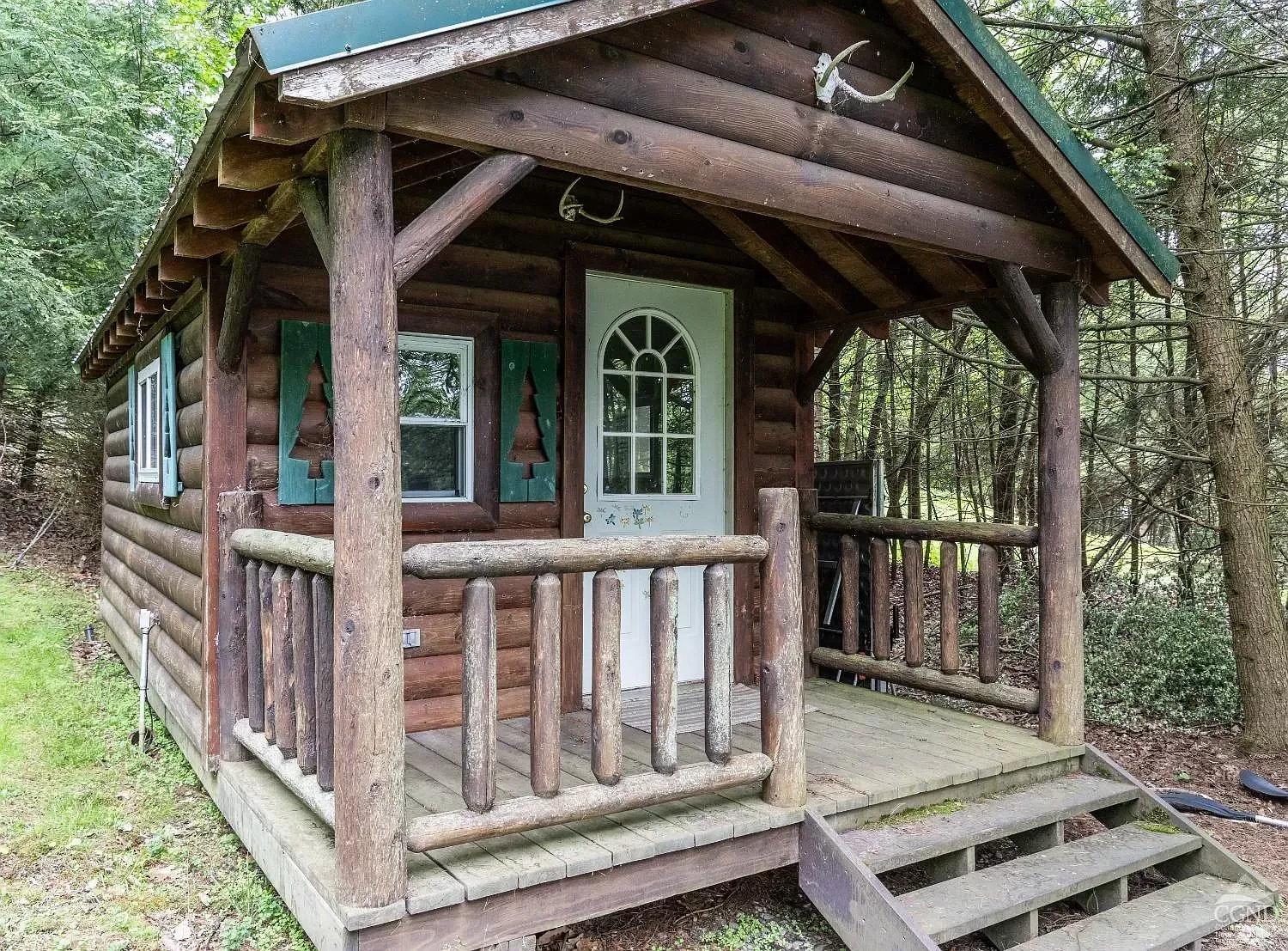 A small log cabin with a porch and stairs in the woods.