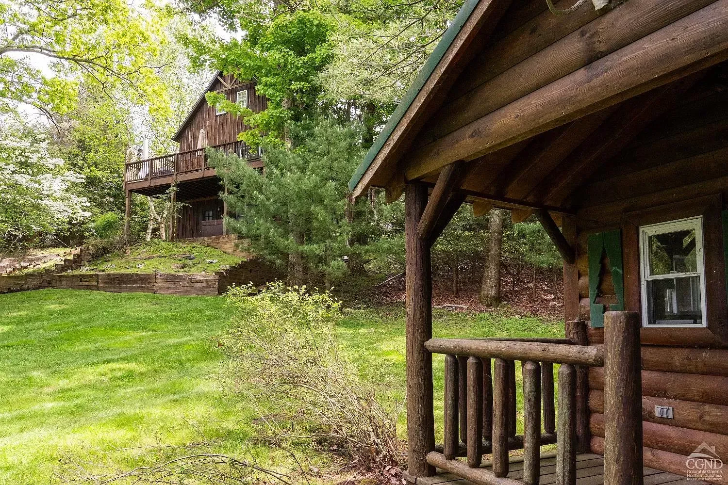 A log cabin with a porch and a deck in the woods.