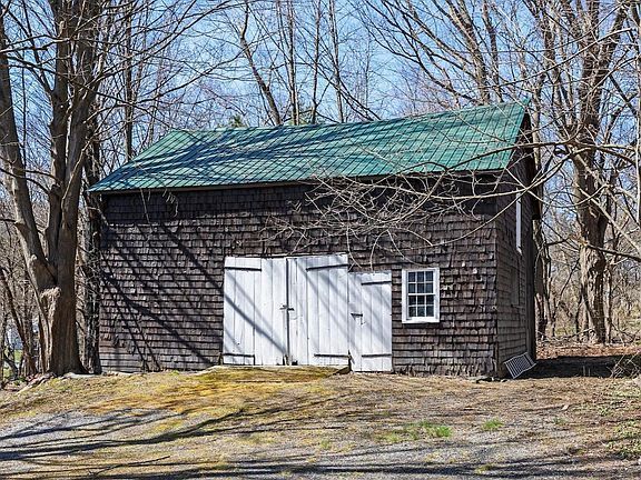 A small barn with a green roof and white doors is surrounded by trees.