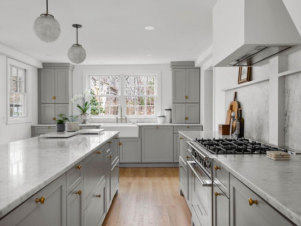 A kitchen with gray cabinets , white counter tops , a stove and a sink.