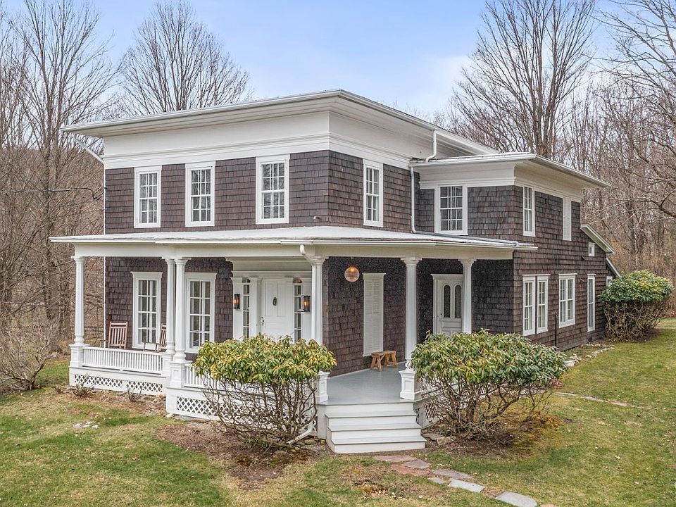 A large brick house with a porch in the middle of a lush green field.