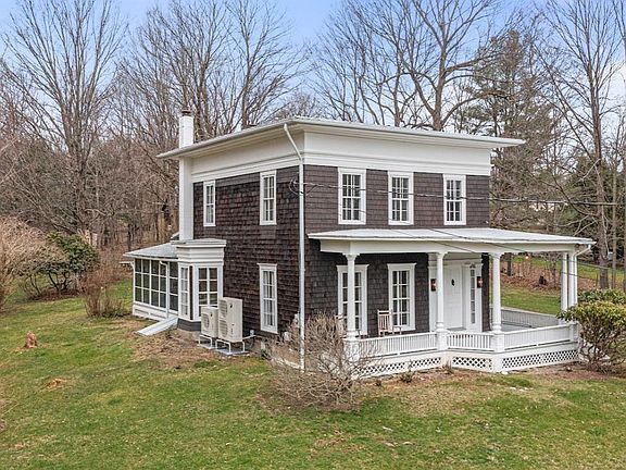 A large brown and white house with a porch in the middle of a grassy field.