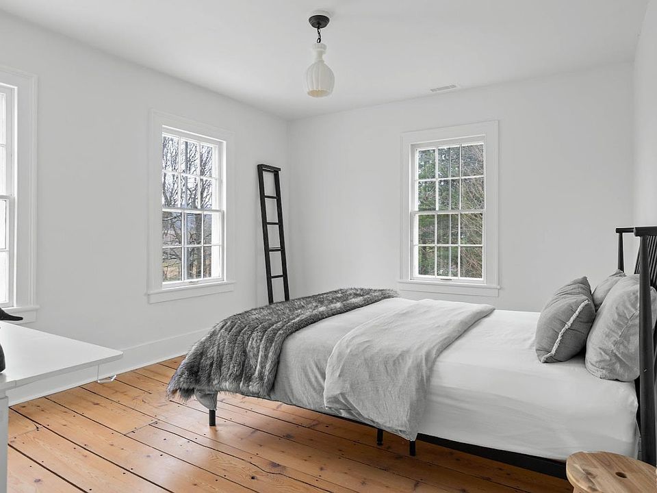A bedroom with a bed , two windows and a wooden floor.
