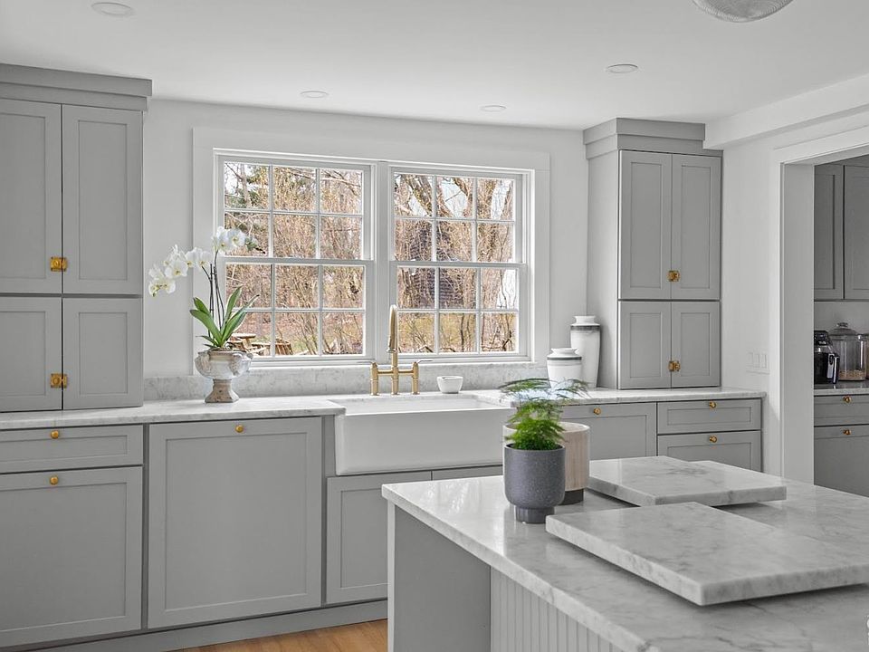 A kitchen with gray cabinets , a white sink , and a large window.