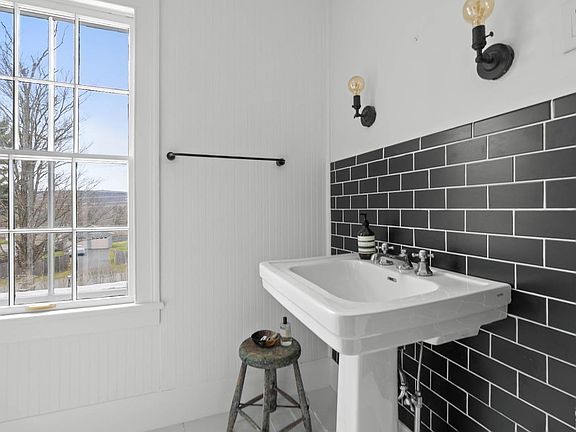 A bathroom with a sink , stool , window and black tiles.