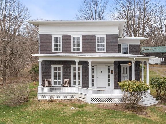 A small brown and white house with a porch in the middle of a field.