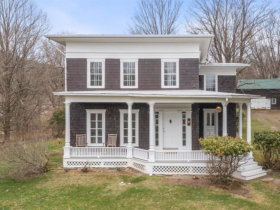 A small brown and white house with a porch and trees in the background.