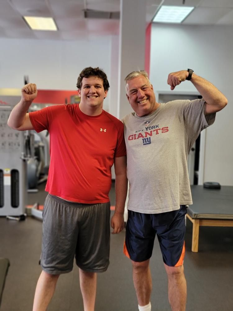 Two men are standing next to each other in a gym and one is wearing a new york giants shirt