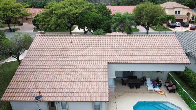 Aerial view of a house with a tile roof, a pool, and a covered patio.