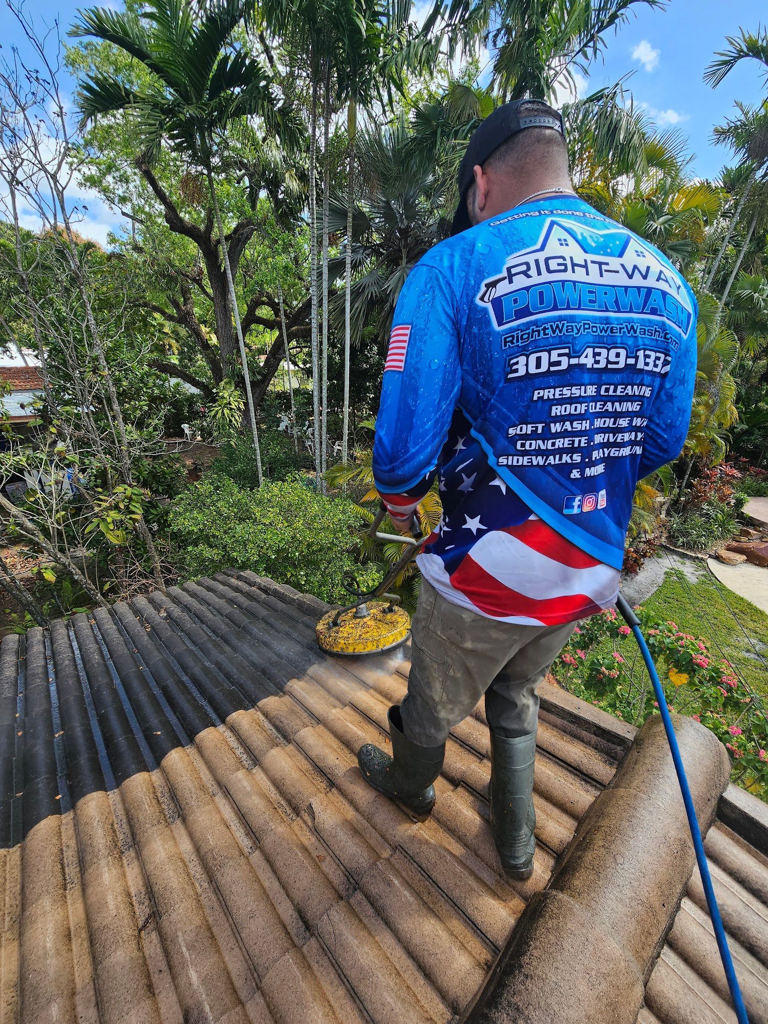 Man power washing a roof wearing a blue shirt with company logo, and the American flag.