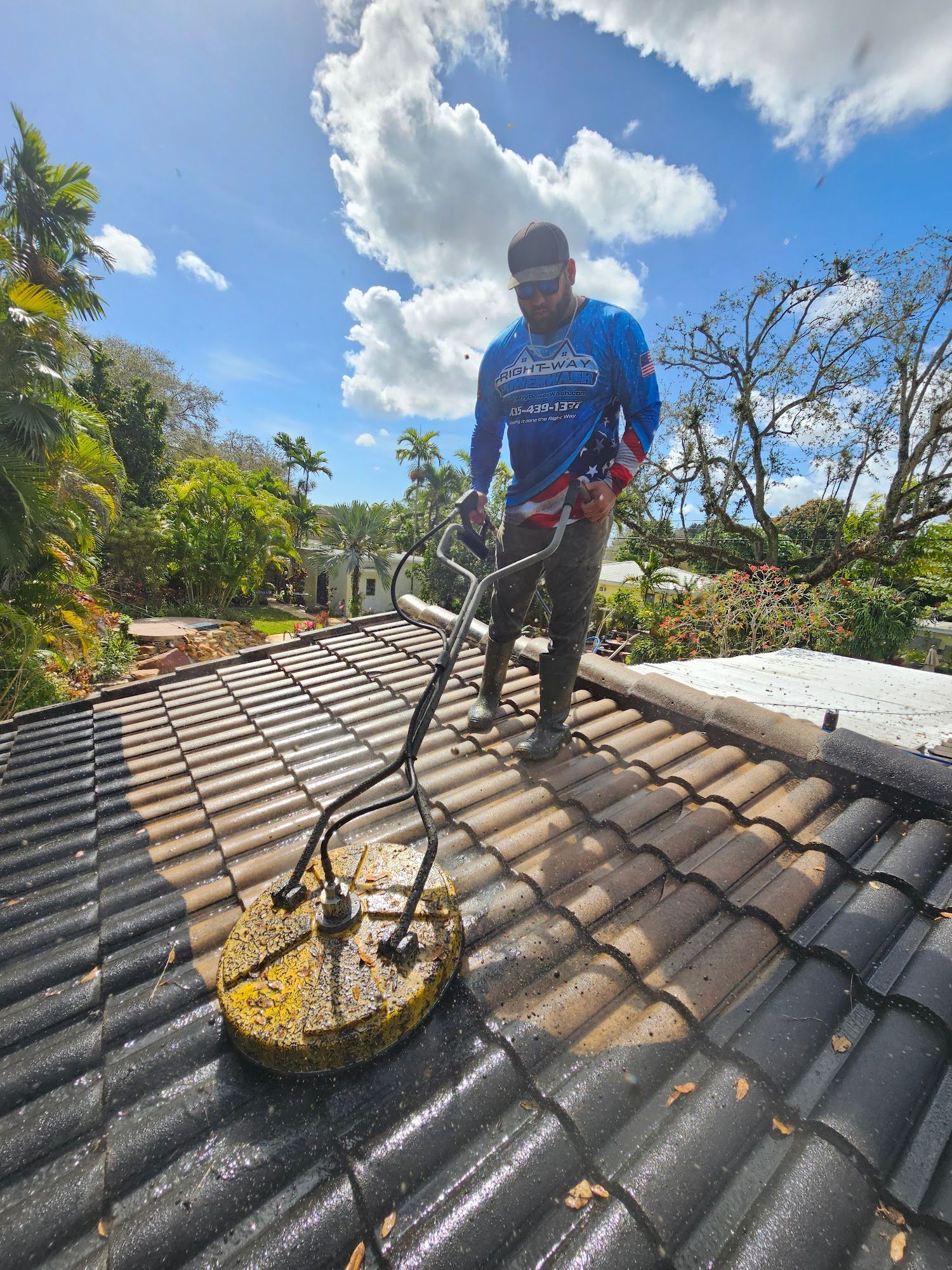 Man pressure washing a tile roof on a sunny day.