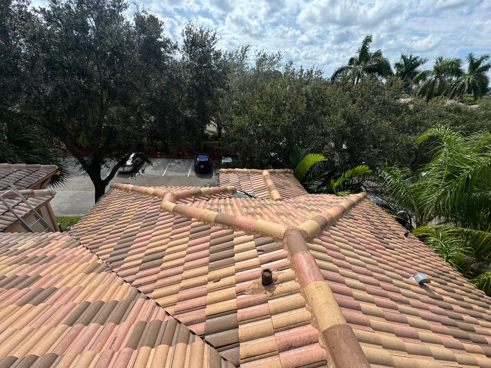 Clay tile roof with trees and parking lot in the background, cloudy sky.