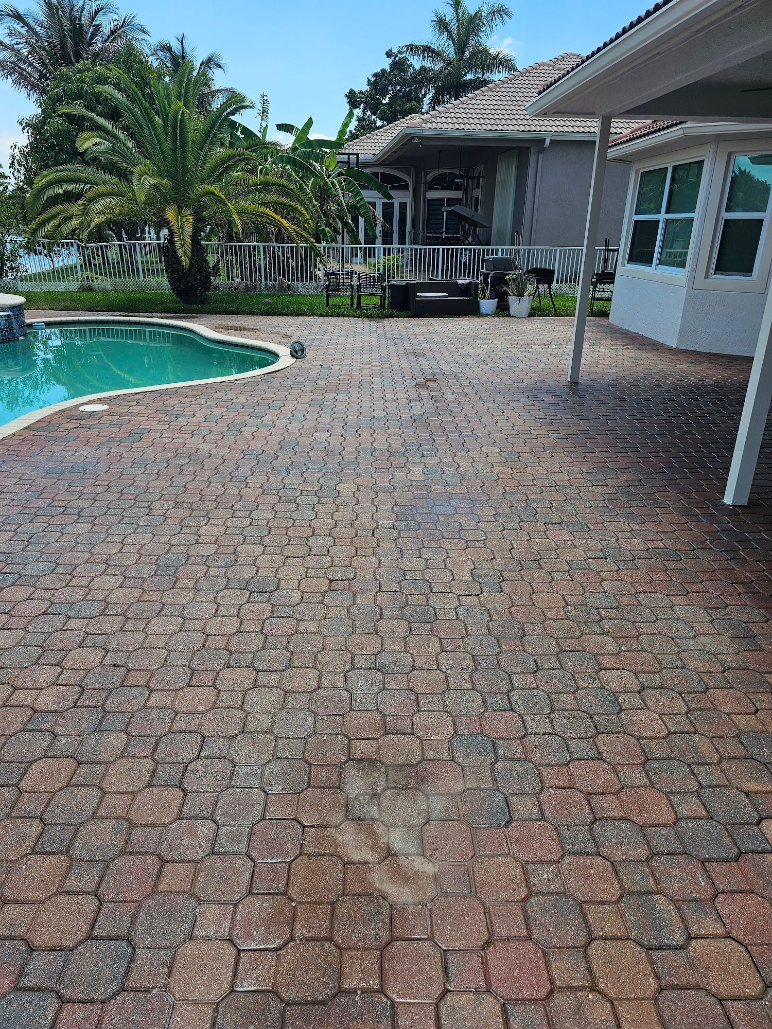 Brick patio next to a pool, with a house in the background.